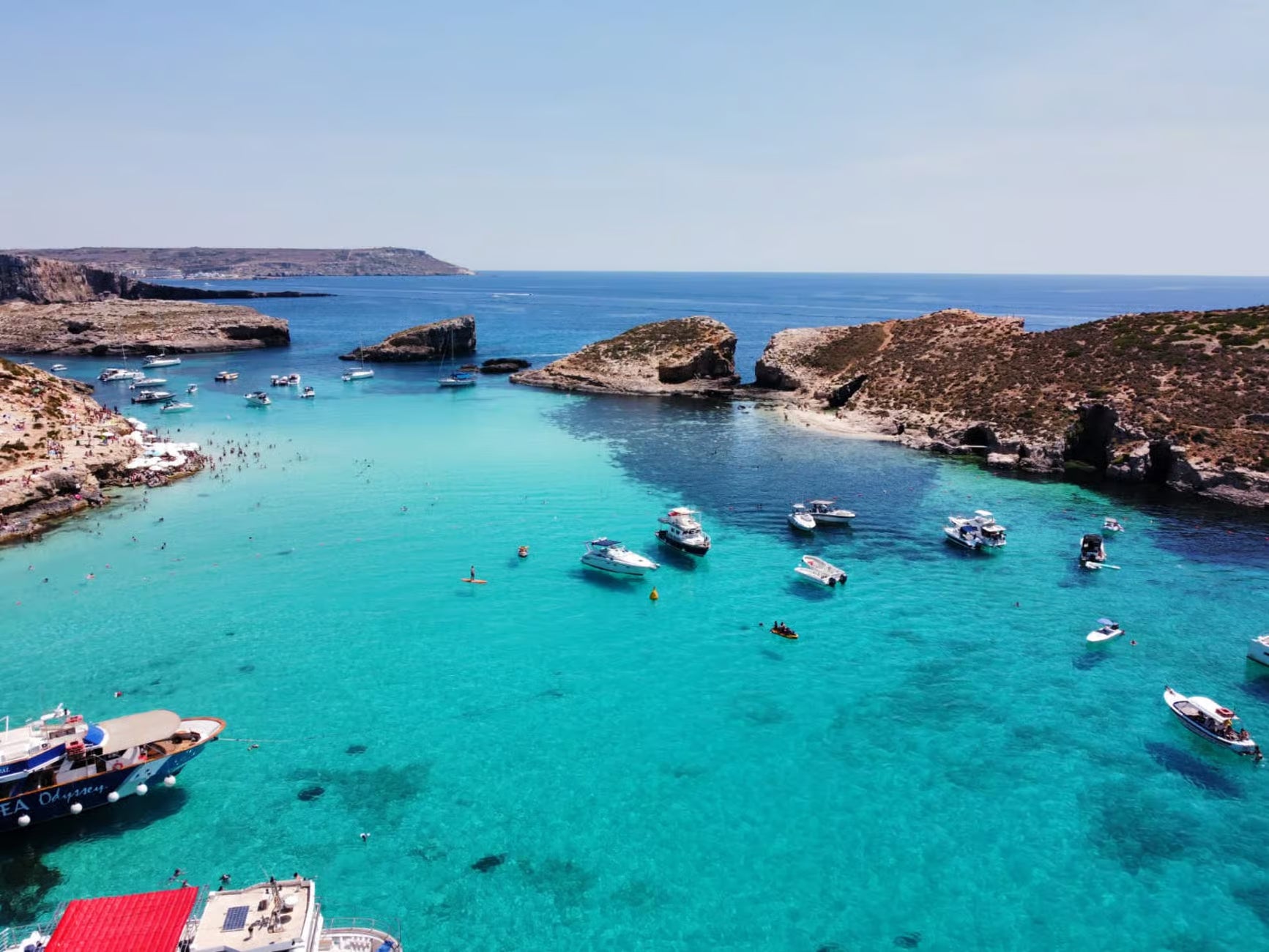 Turquoise waters with boats and rocky cliffs under a clear blue sky