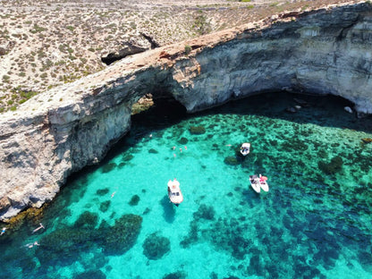 Cave entrance with clear blue water and boats near a rocky coastline