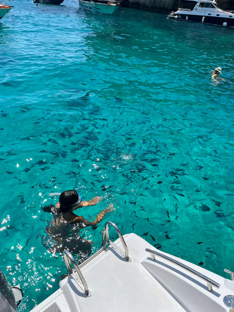 Person swimming in clear blue water with boats in the background