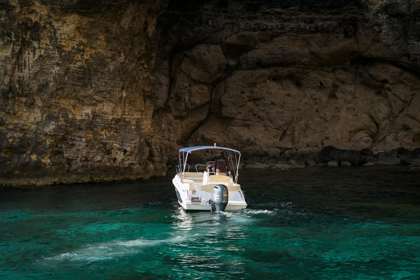 Boat navigating through a narrow cave entrance in clear blue water