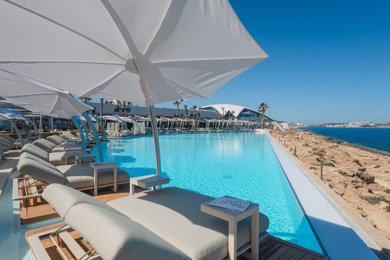 Sunbeds and white umbrellas by the infinity pool at Café del Mar Malta on a summer day