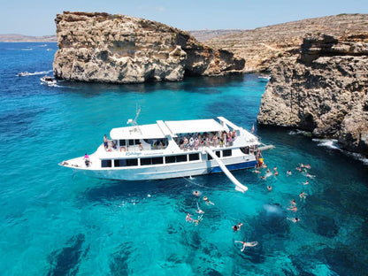 Boat with people enjoying the clear blue water near rocky cliffs