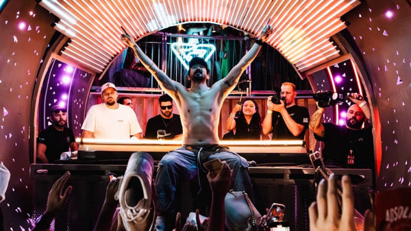 Person with arms raised in a celebratory manner at a party with disco ball and colorful lights.