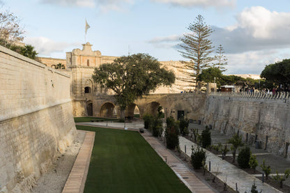 Historic stone walls with a garden and trees under a blue sky.
