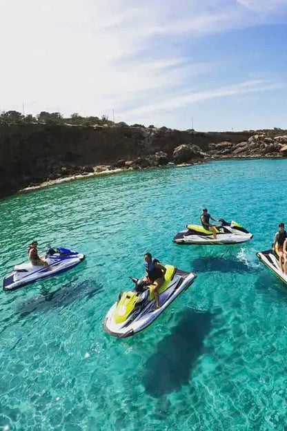 People enjoying jet skiing in clear blue water near a rocky coastline.