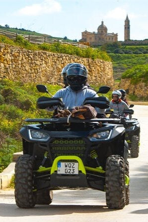 People riding ATVs on a scenic road with a historic building in the background